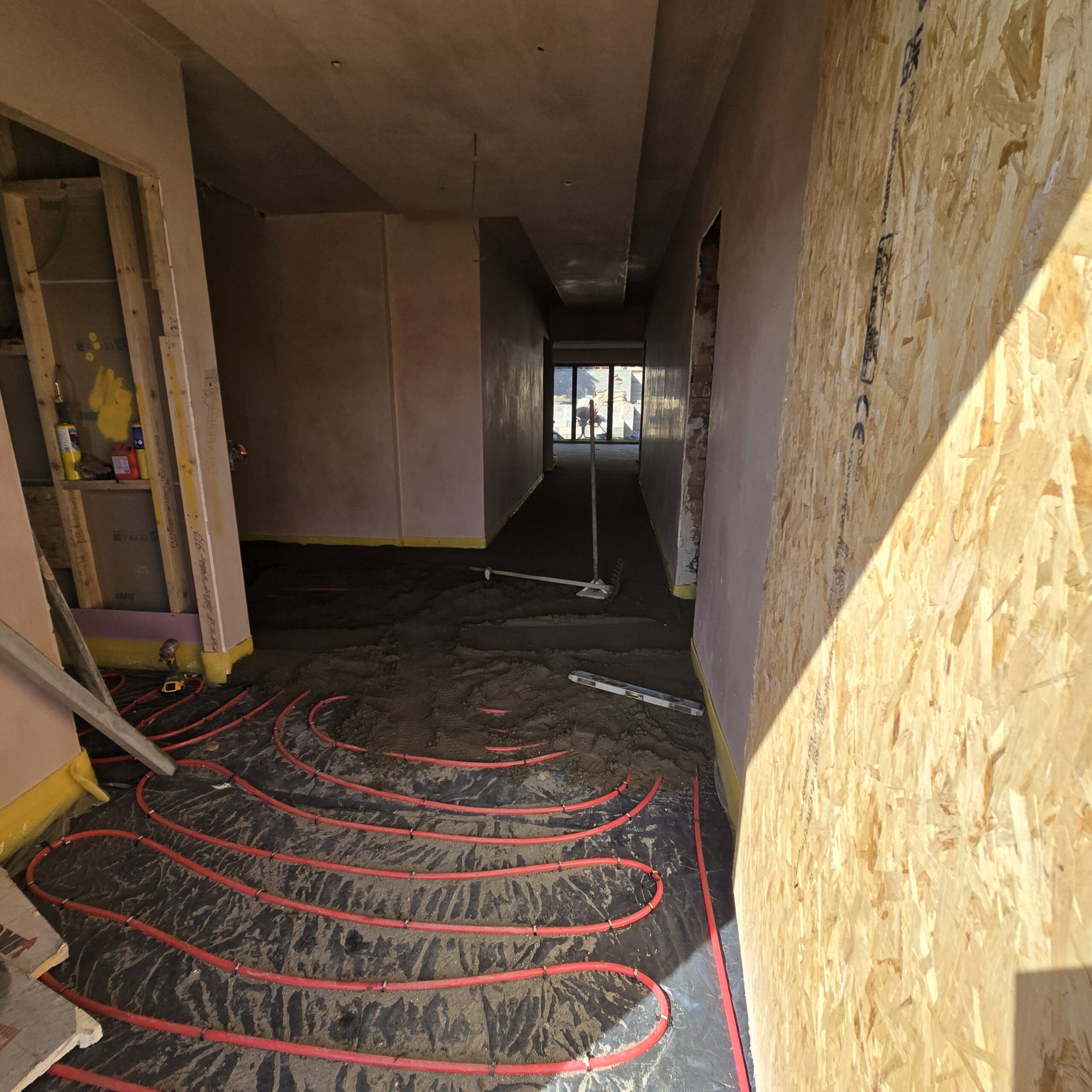 Red water underfloor heating pipes laid across a floor before screed installation by KWS Builders Manchester